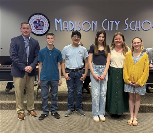Four Discovery Middle band students with principal and band director standing in front of the Board meeting